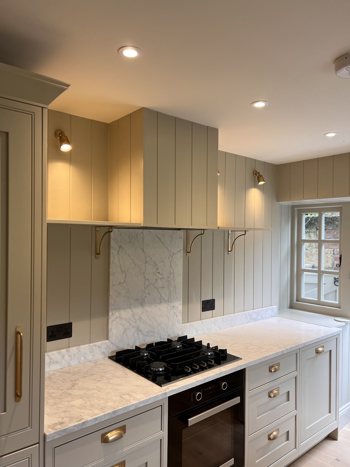 Shaker kitchen with brass picture lights and downlights over marble